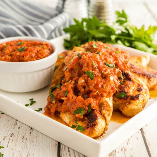 chicken romesco on a plate with a bowl of extra sauce and parsley
