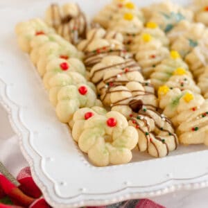A plate of assorted spritz cookies, made from a classic spritz cookie recipe, decorated with chocolate drizzle, colored sugar, red candies, and star-shaped sprinkles.