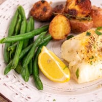 baked fish with lemon on a white plate with vegetables