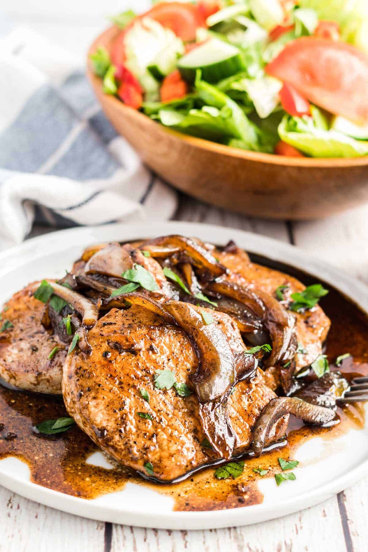 Balsamic Glazed Pork Chops on a white plate, with a bowl of salad
