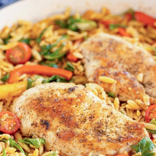 cooked chicken breasts in a skillet with orzo.