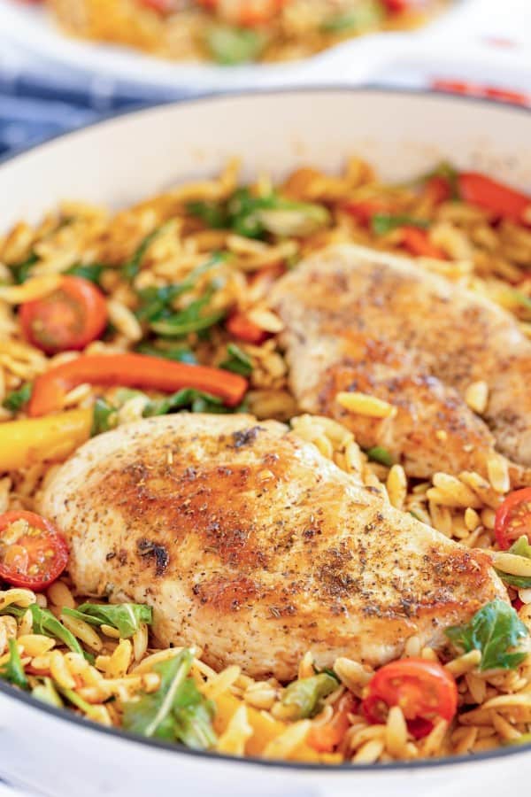 cooked chicken breasts in a skillet with orzo.