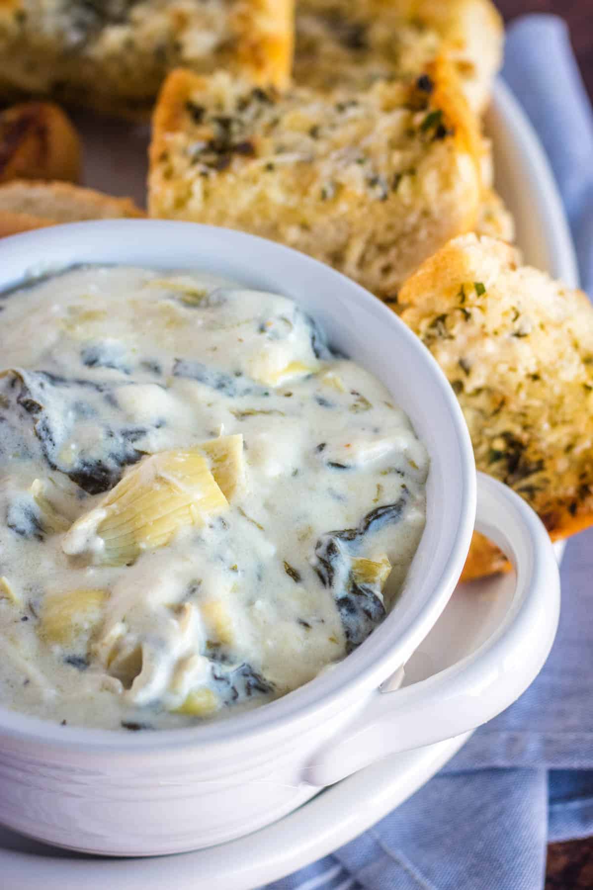 spinach artichoke dip in a white bowl with garlic bread toast