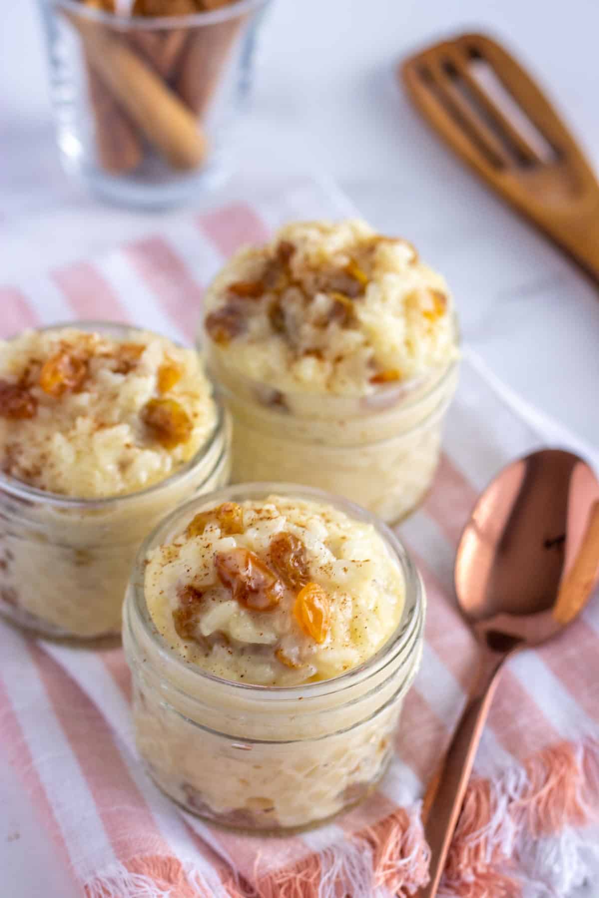 rice pudding in glass jars with a rose gold spoon and a pink and white napkin