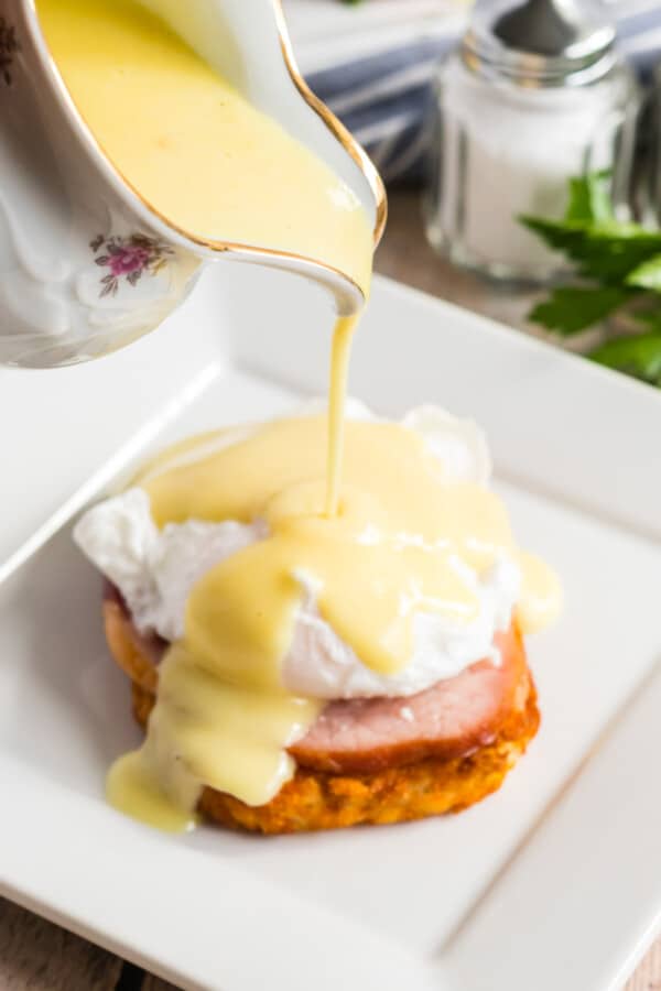 hollandaise sauce being drizzled onto eggs benedict