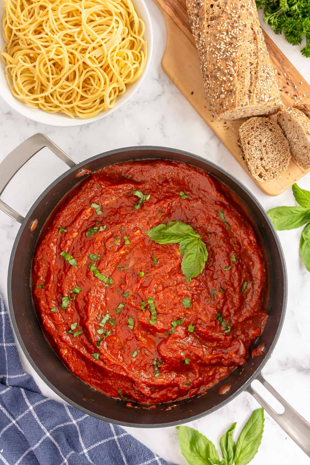 marinara sauce in a skillet with basil, bowl of spaghetti and bread on the side