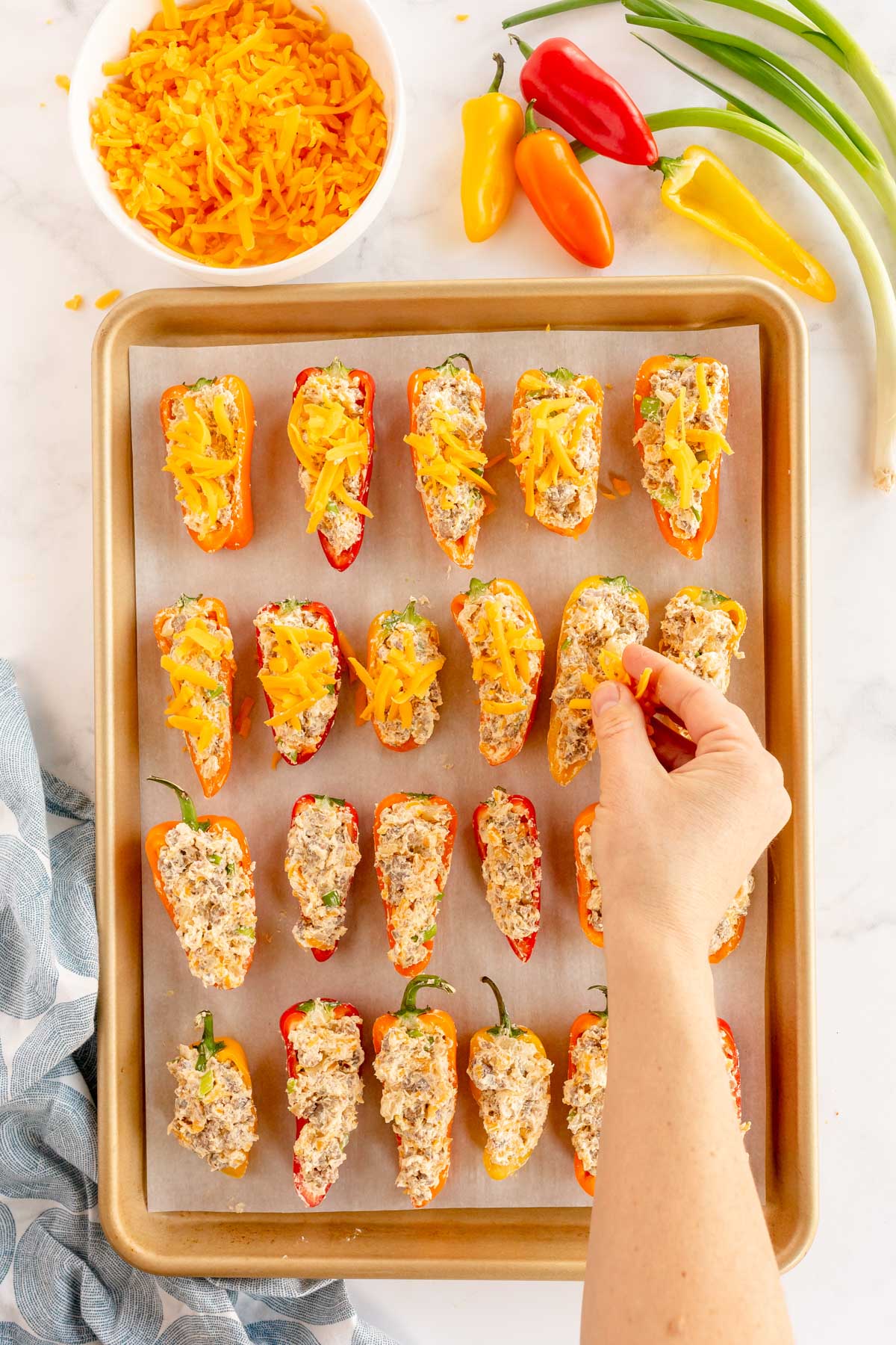 sprinkling cheese on stuffed mini peppers on a baking sheet