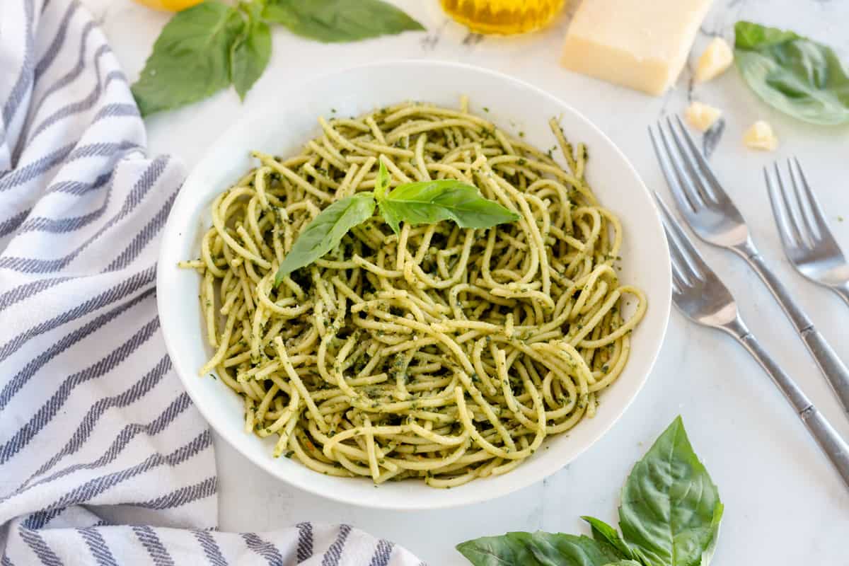 spaghetti with basil pest in a white bowl with forks and a stripe linen