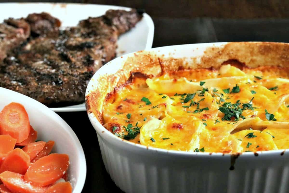 scalloped potatoes in a baking dish with steaks and carrots