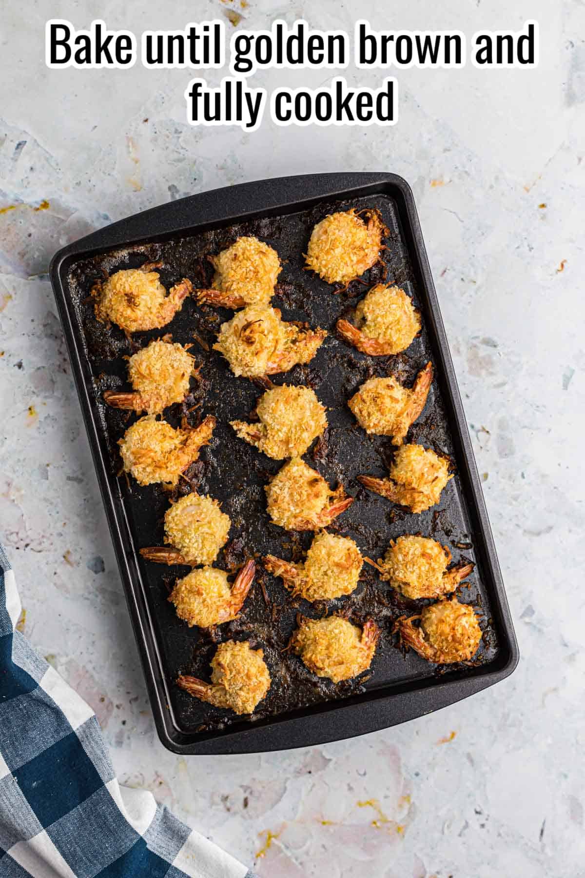 fully cooked coconut shrimp on a black sheet pan.