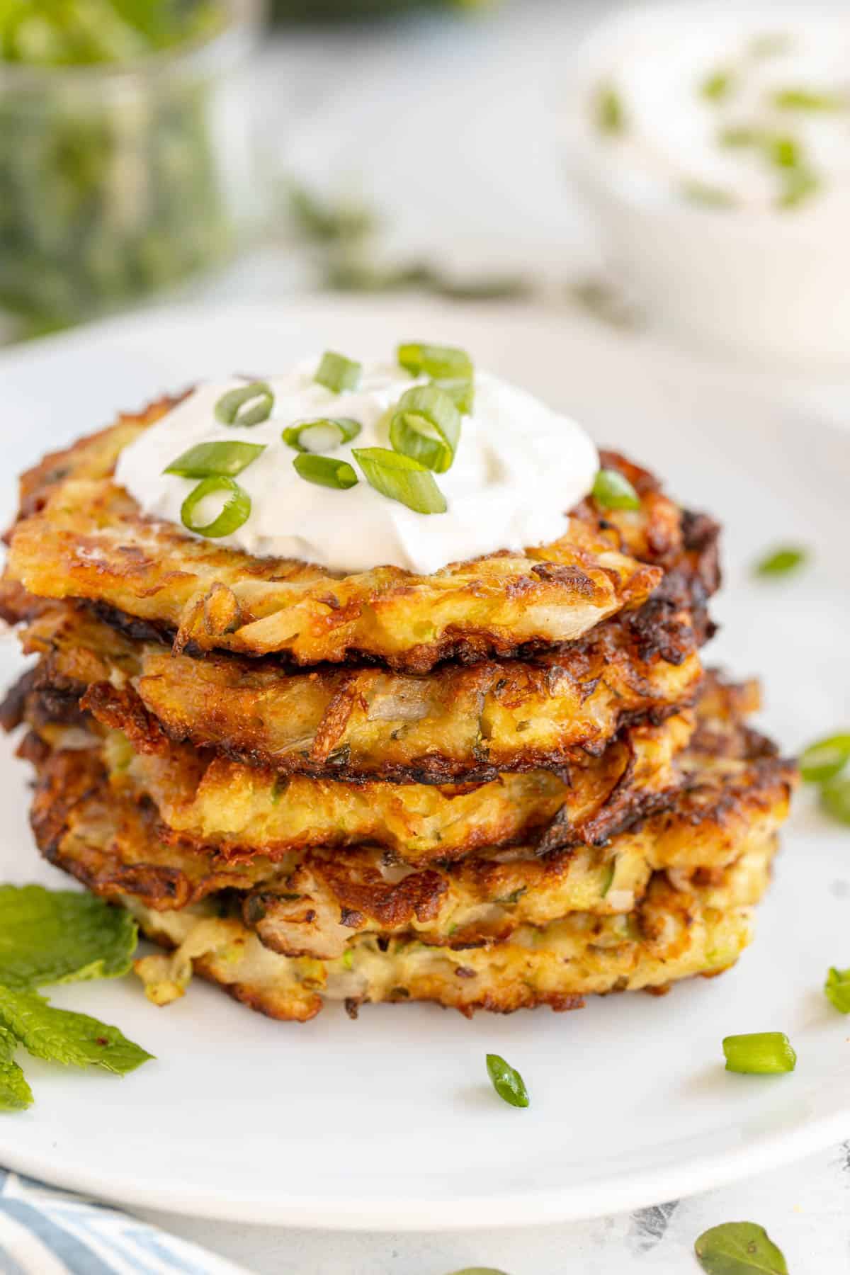 zucchini fritters stacked on a plate with sour cream and green onions on top 