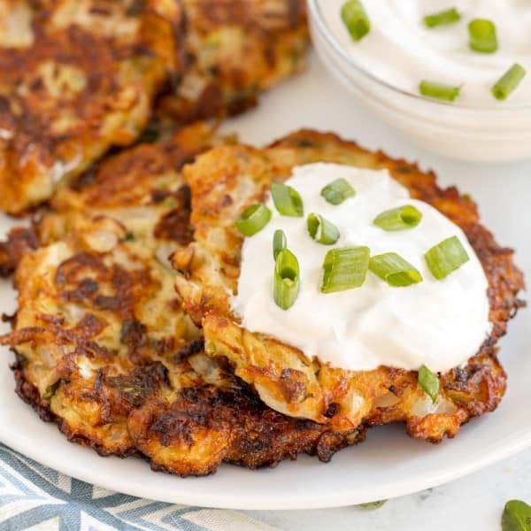 zucchini fritters on a white plate on a plate with sour cream and green onions on top.