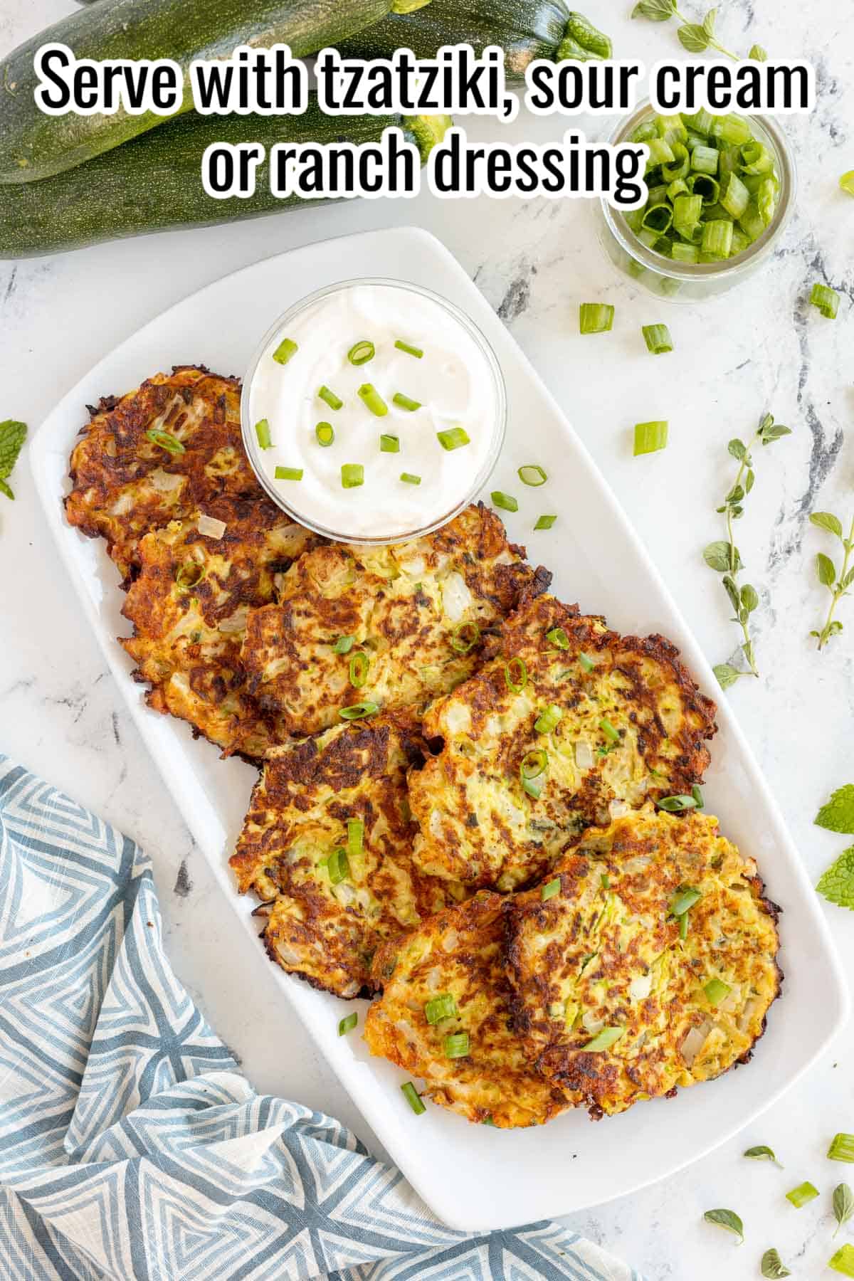 cooked zucchini fritters on a platter with a bowl of sour cream