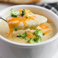 broccoli cheddar soup with a spoon out of the soup and bread in the background