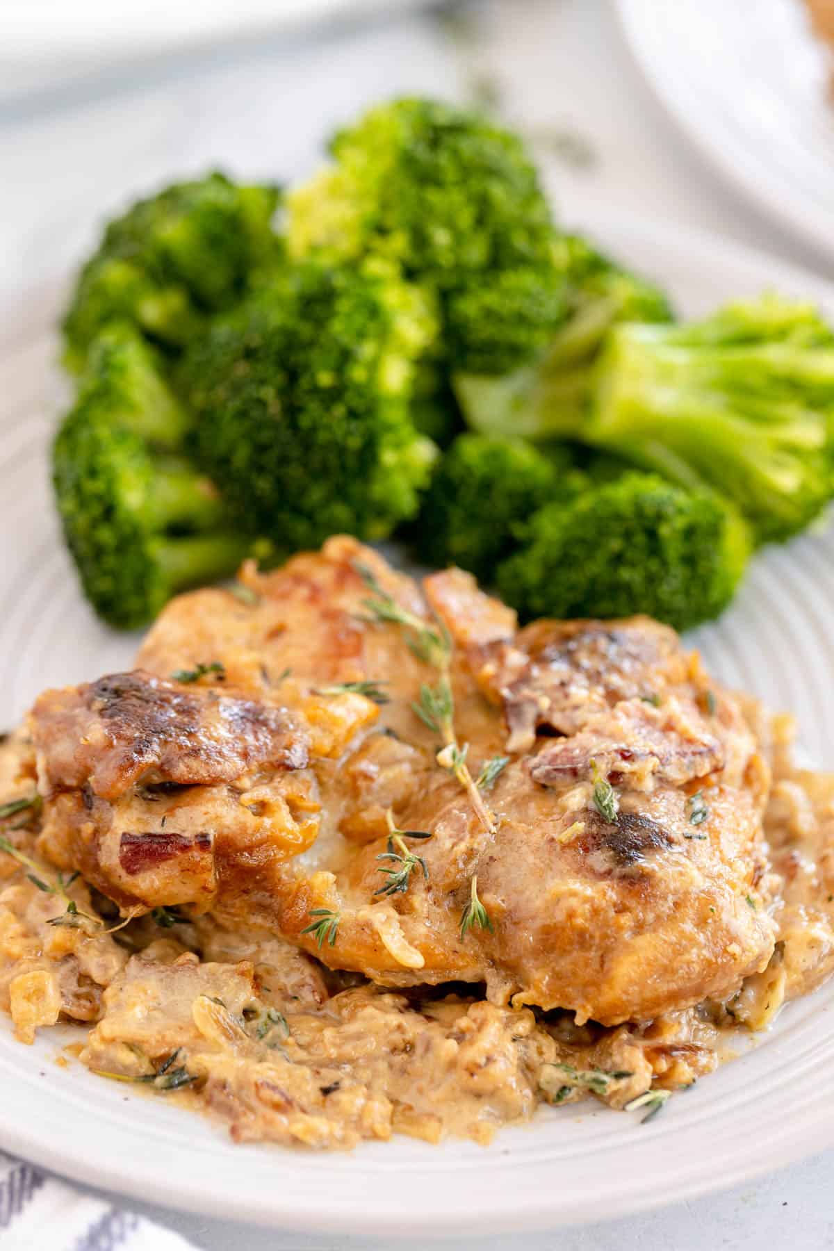 smothered chicken on a white plate with broccoli.