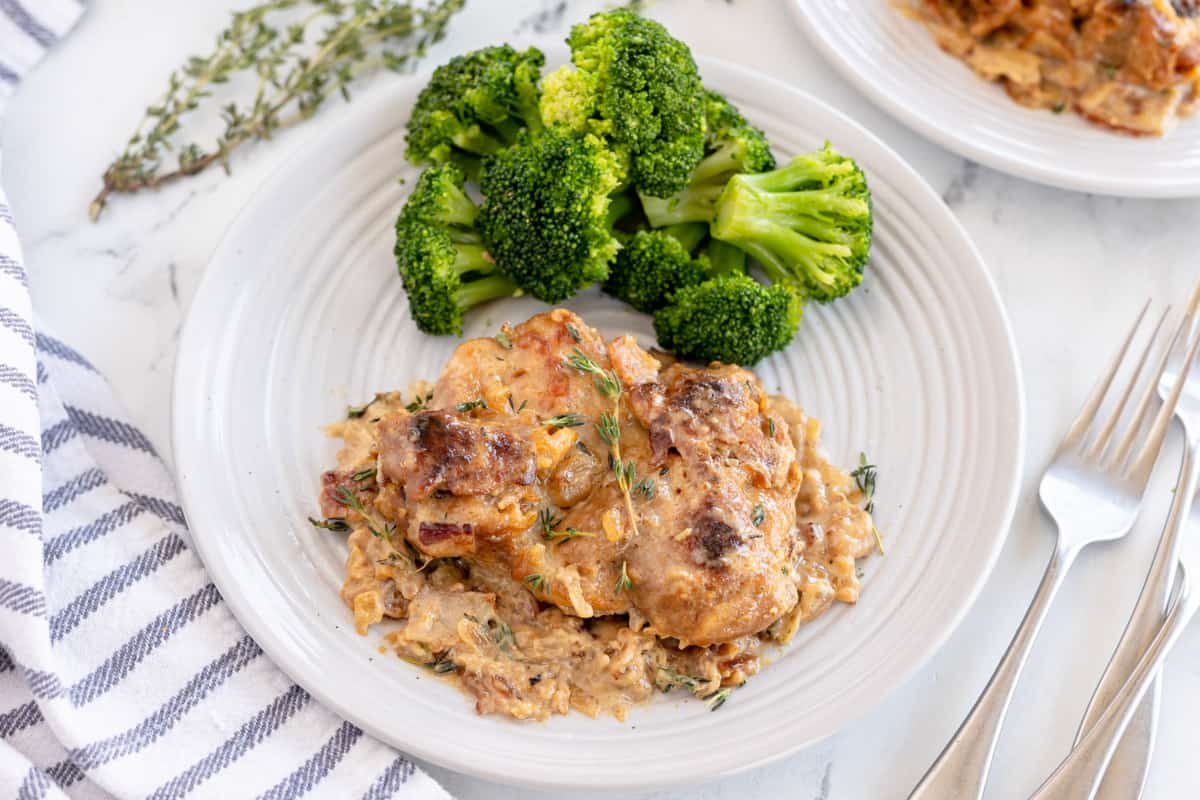 chicken with gravy on a white plate with broccoli.