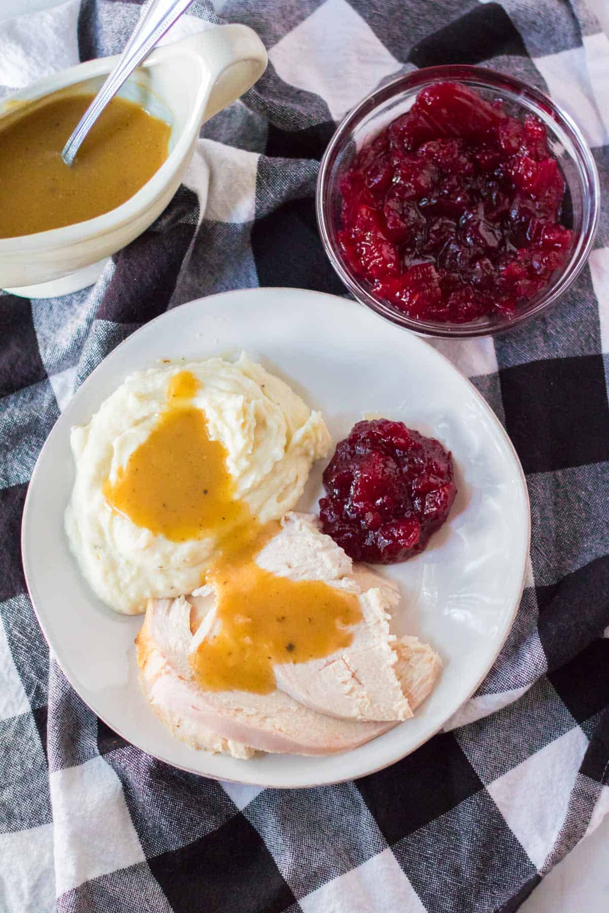 Slow Cooker Turkey Breast that is sliced, and on a plate with gravy and cranberry sauce.
