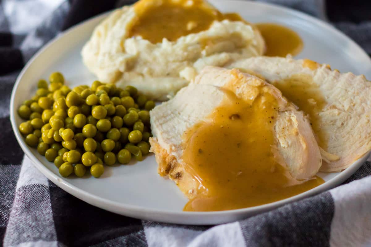 white plate with peas, mashed potatoes and turkey with gravy.