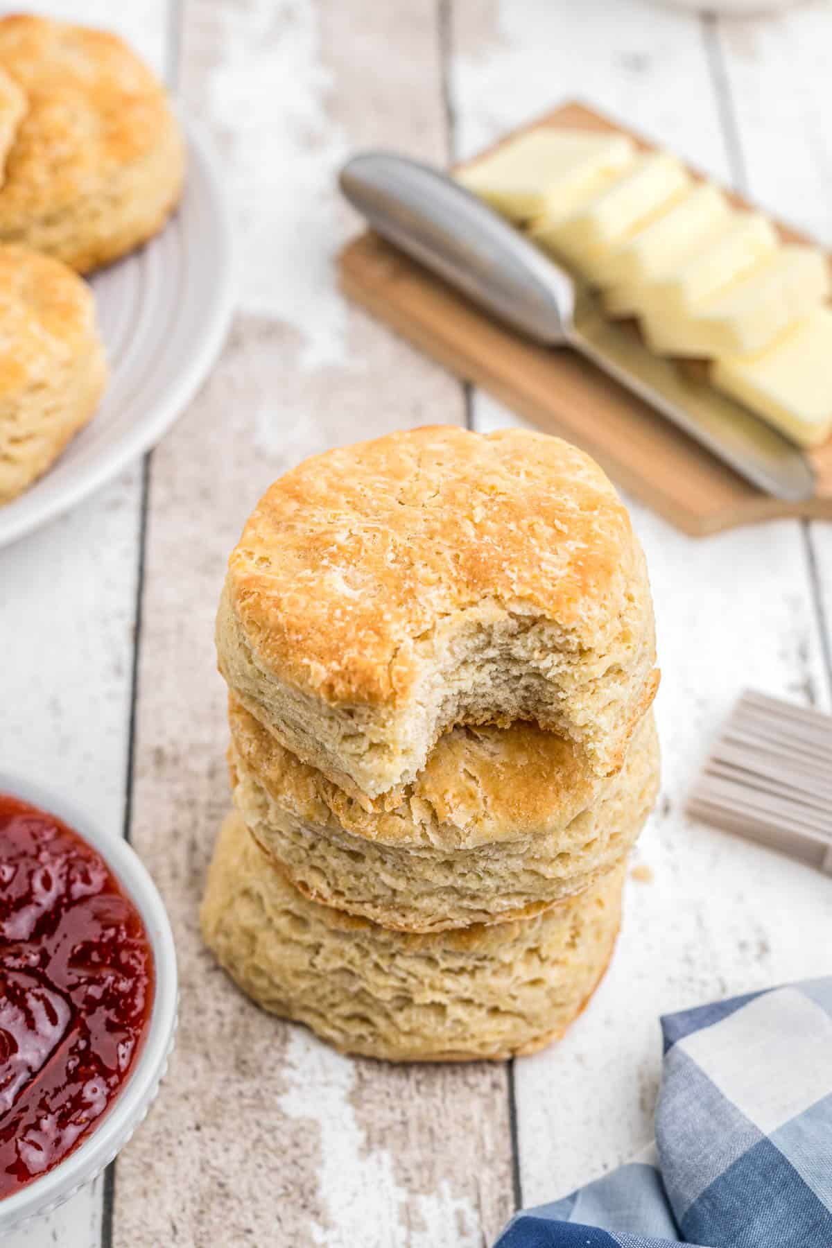 Buttermilk biscuits with butter and jam stacked on a white background.