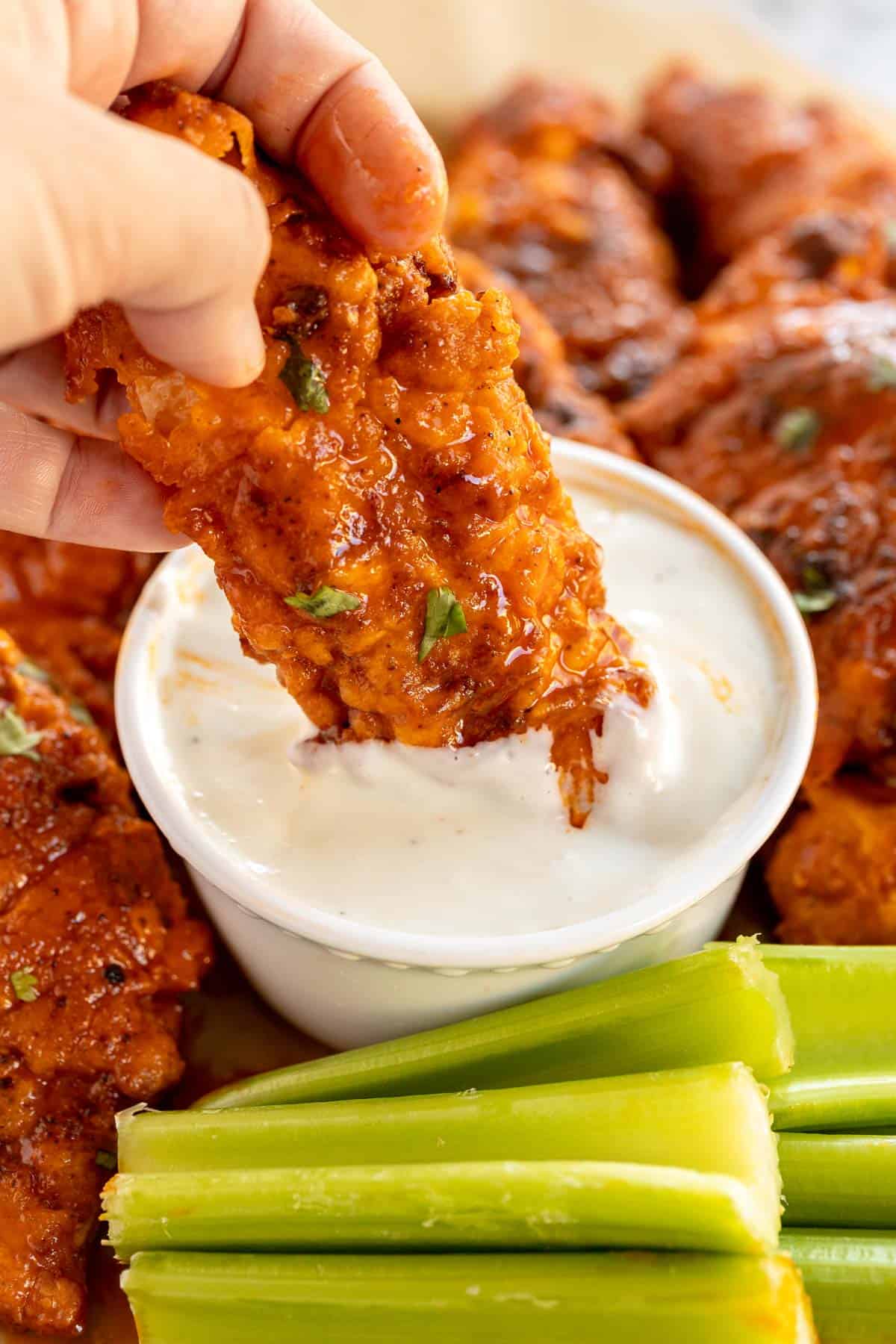 buffalo chicken tender being dipped in ranch dresssing.