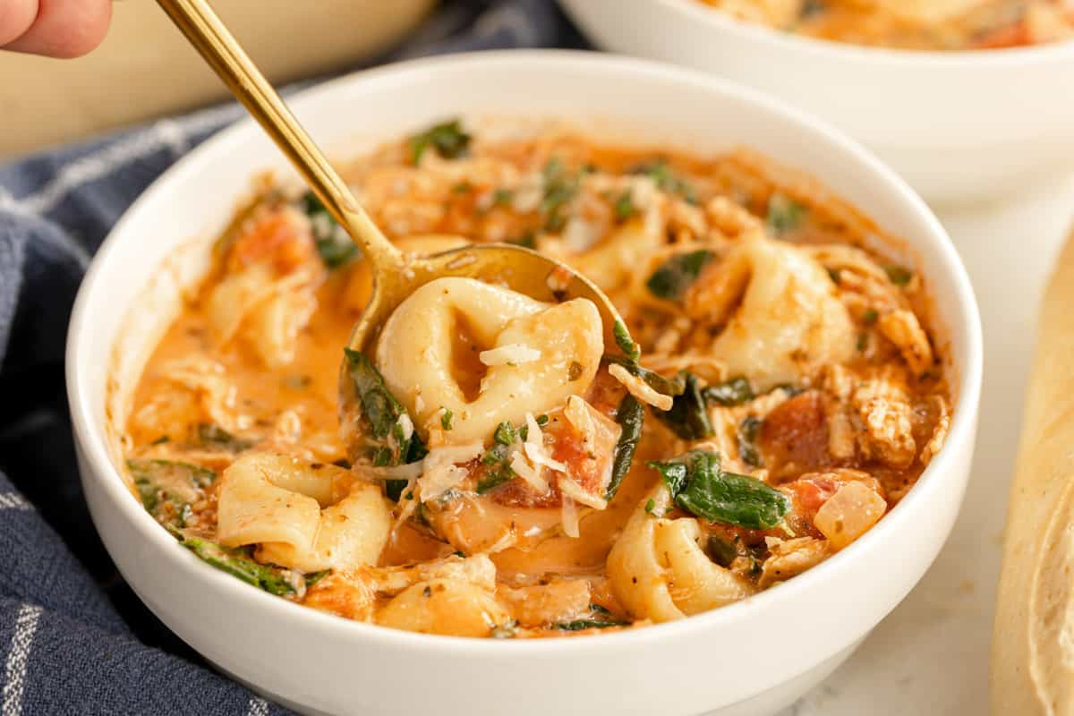 Chicken tortellini soup in a bowl with a spoon.