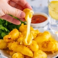 hand holding a fried cheese curd with stretchy cheese.