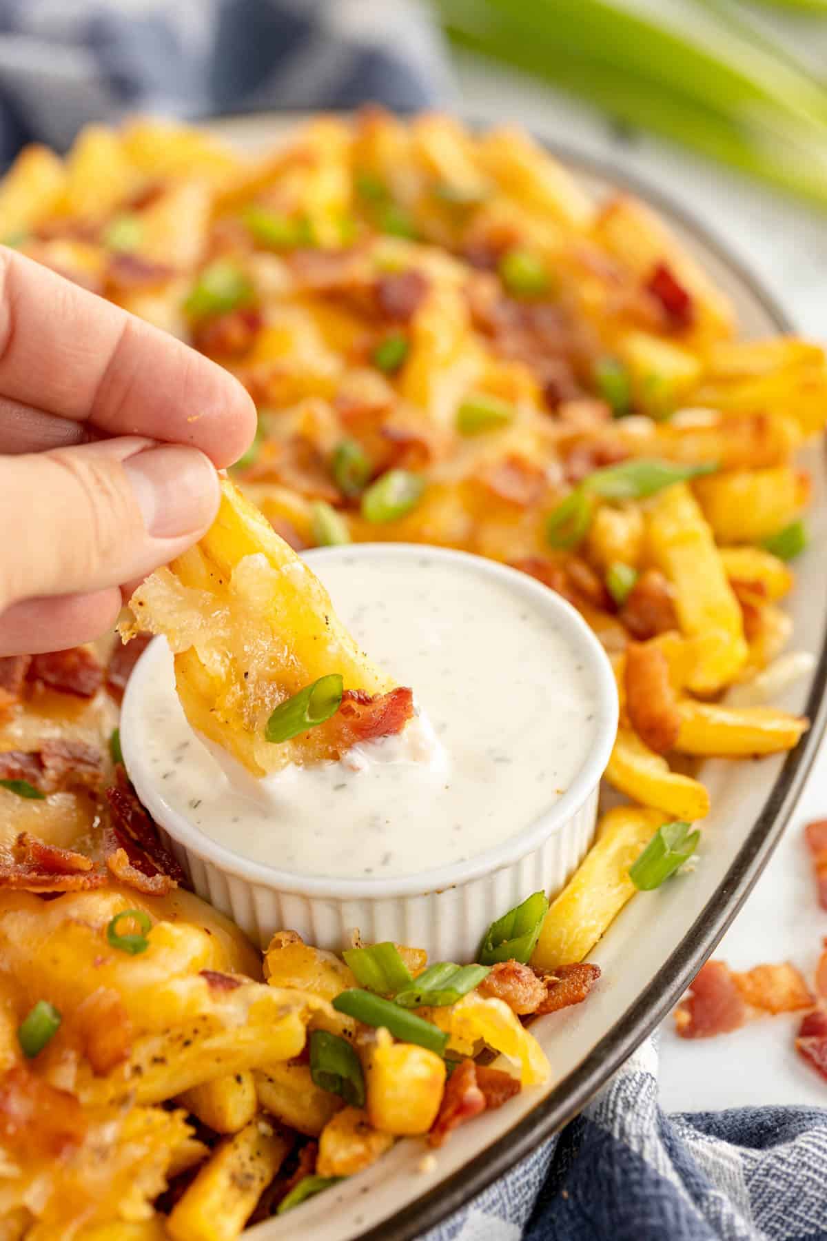 loaded cheese fries on a platter with a hand dipping intoranch dip.