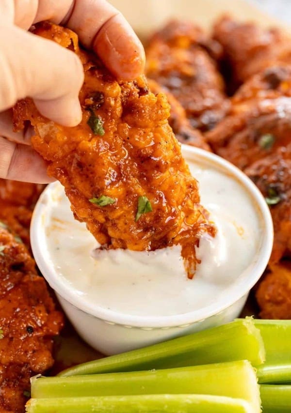 buffalo chicken tender being dipped in ranch dresssing.