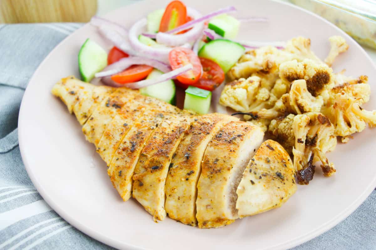 sliced chicken breast on a white plate with salad.