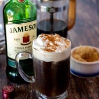 Irish coffee with a whiskey bottle, sugar and coffee in the background