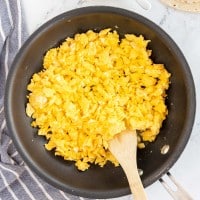 scrambled eggs in a skillet with a wooden spoon.