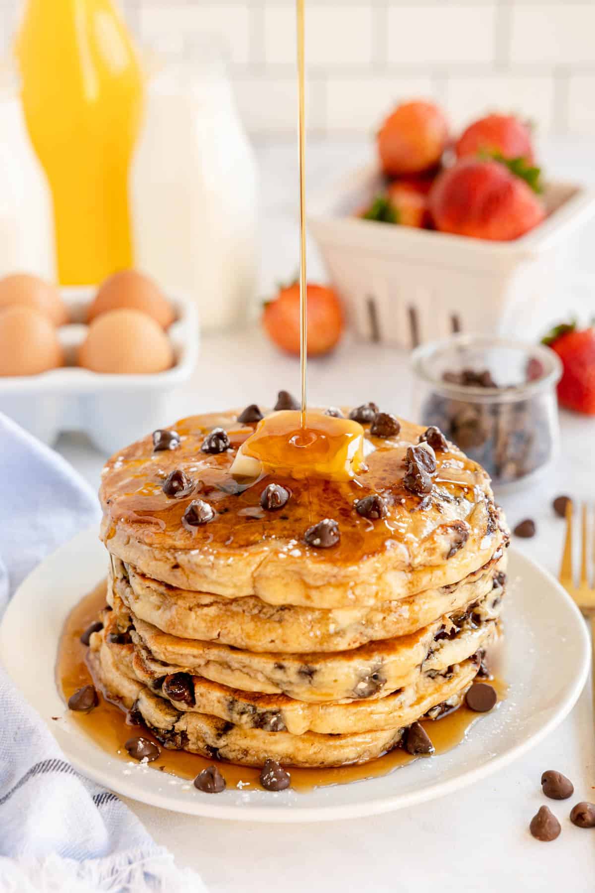 chocolate chip pancakes on a white plate with maple syrup being drizzled.