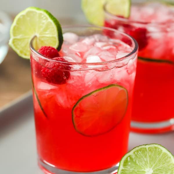 raspberry limeade in two glasses on a tray with limes.