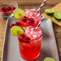 raspberry limeade in two glasses on a tray with limes.