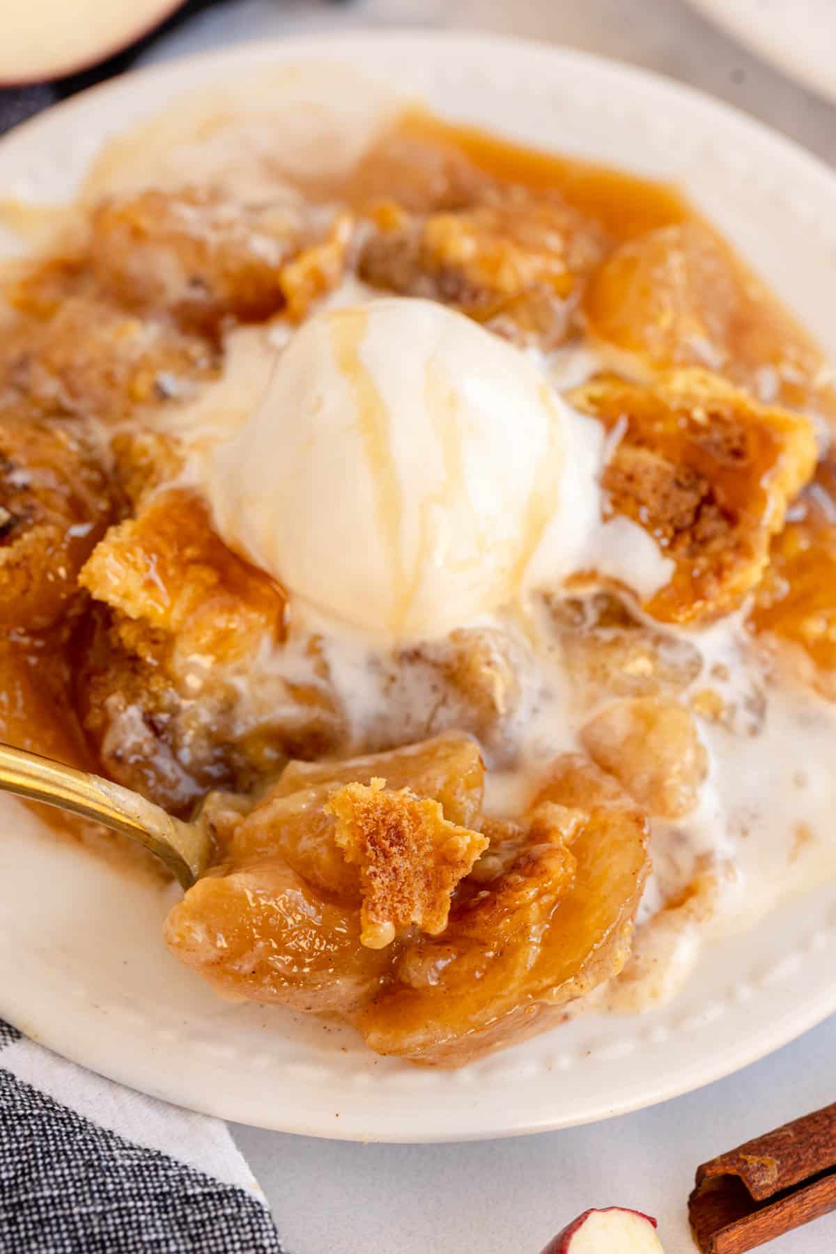 A plate of apple dump cake with ice cream and cinnamon sticks.