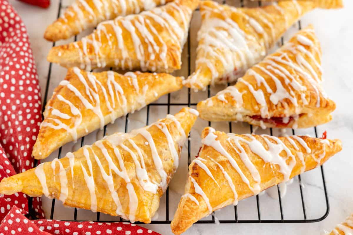 Strawberry turnovers with icing on top cooling on a wire rack.