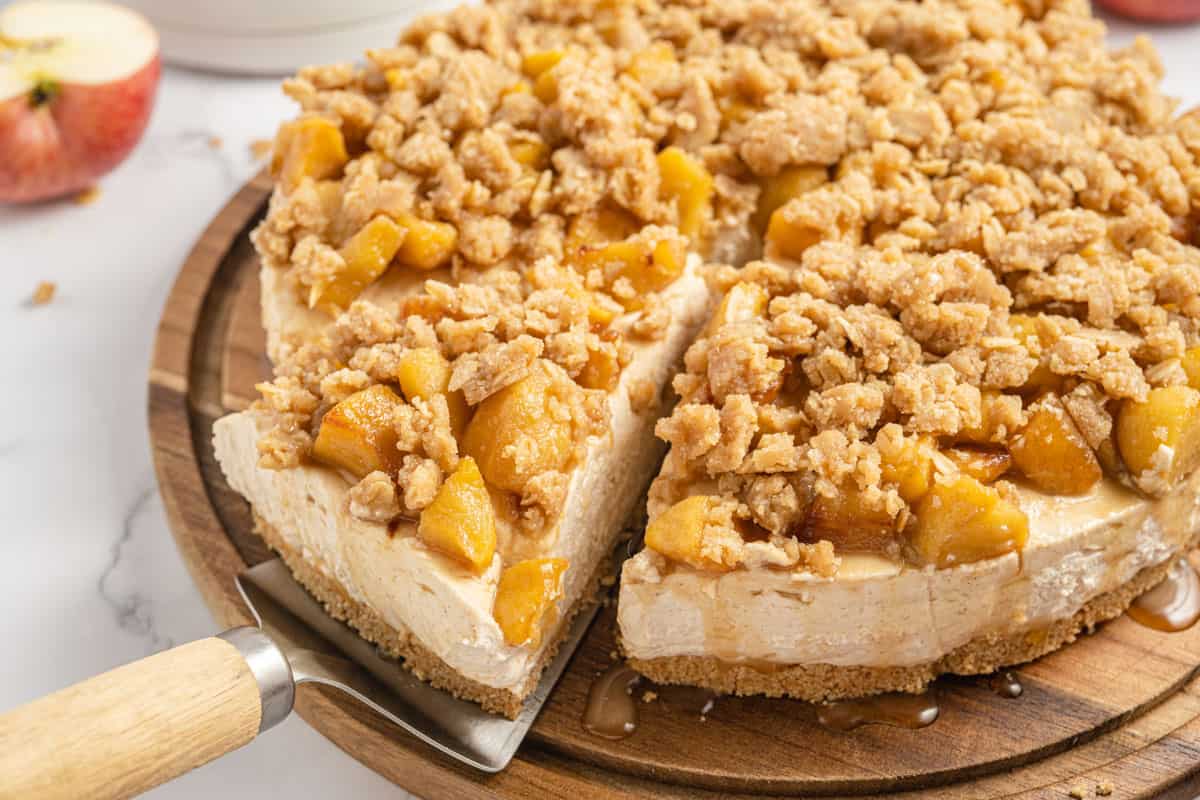 A slice of apple crumble cheesecake on a wooden cutting board.