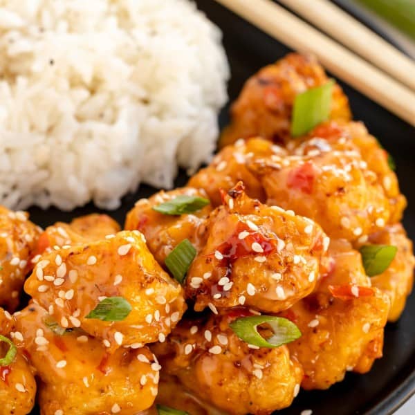 Bang bang chicken with rice and sesame seeds on a plate with chopsticks.