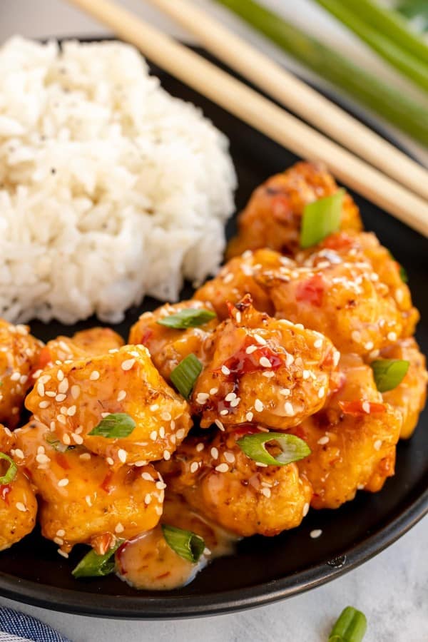 Bang bang chicken with rice and sesame seeds on a plate with chopsticks.