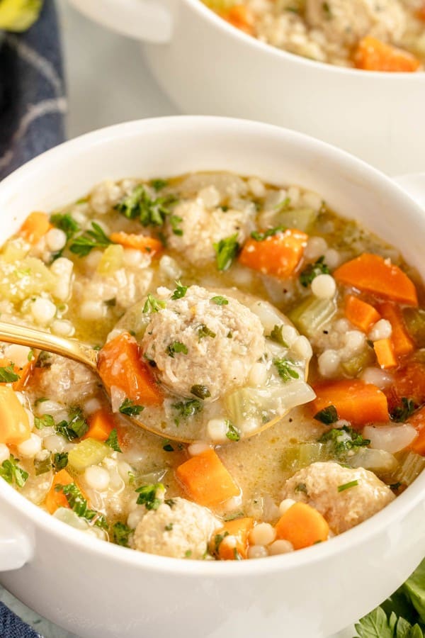 A bowl of meatball soup with carrots and parsley.