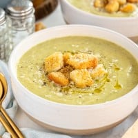 Bowls of Zucchini Soup with zucchini and salt and pepper shakers.
