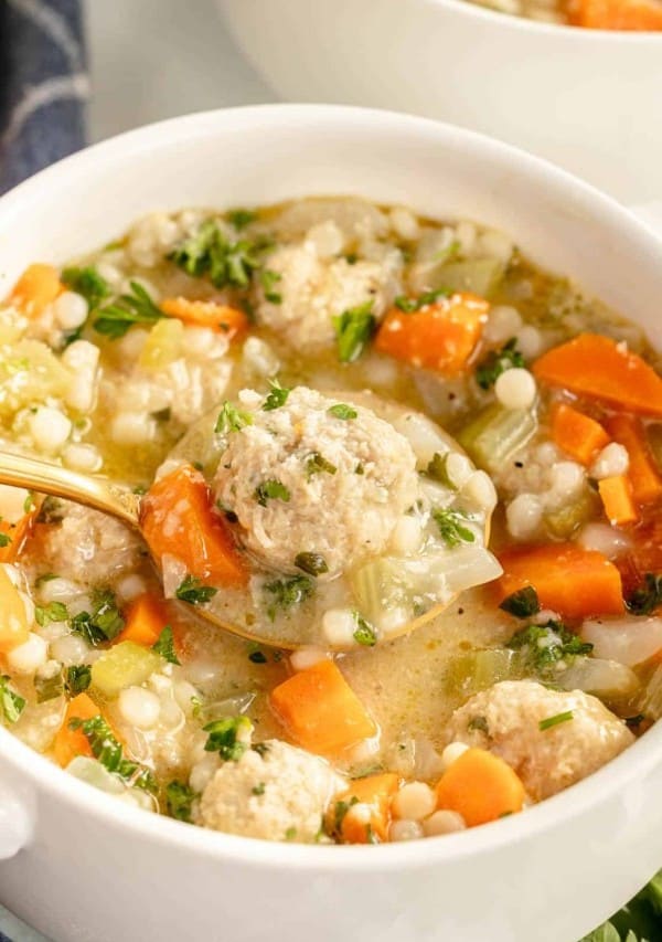 A bowl of meatball soup with carrots and parsley.