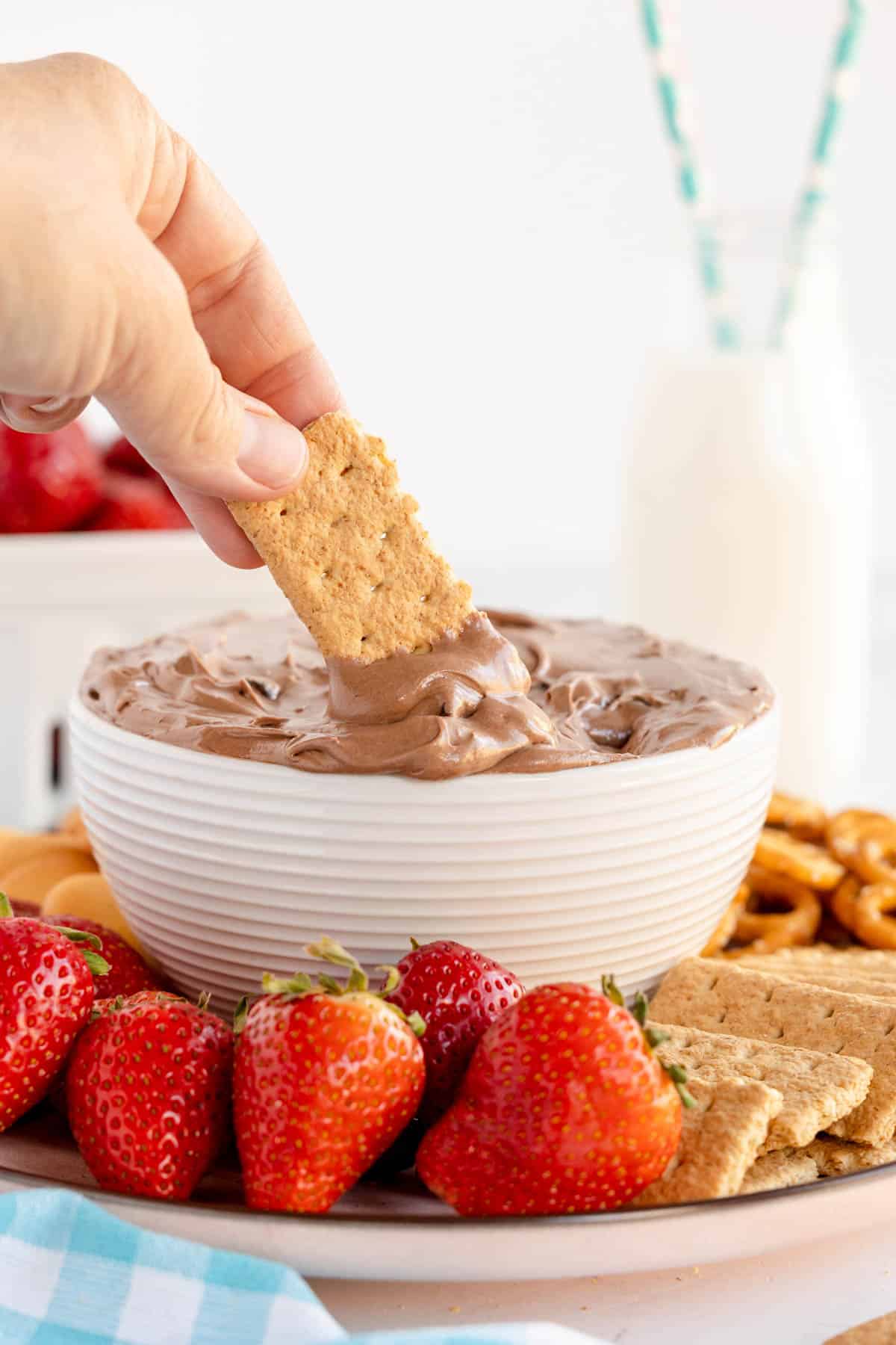 bowl of brownie batter dip with a hand holding a graham cracker.