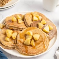 A plate of pancakes with apples and syrup on it.