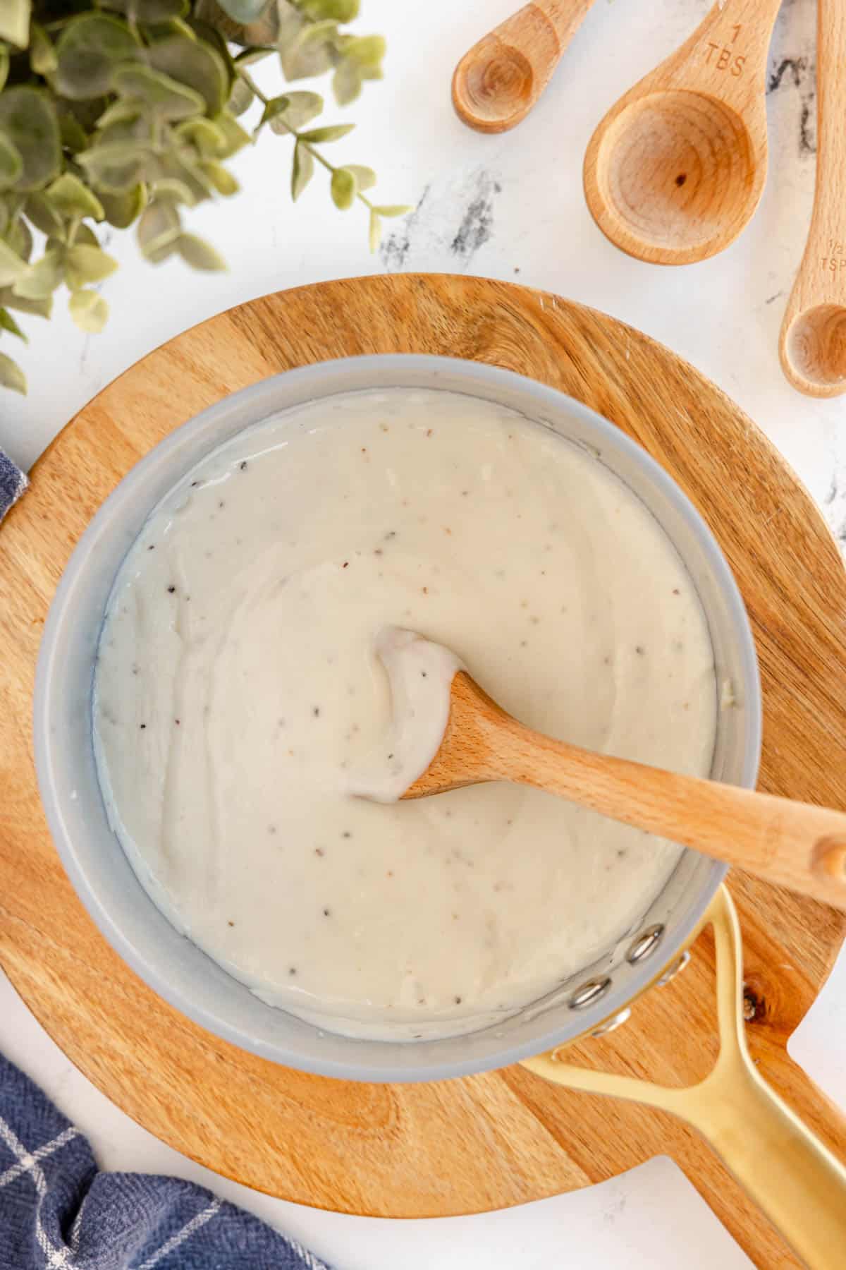 a white sauce in a saucepan with a wooden spoon.