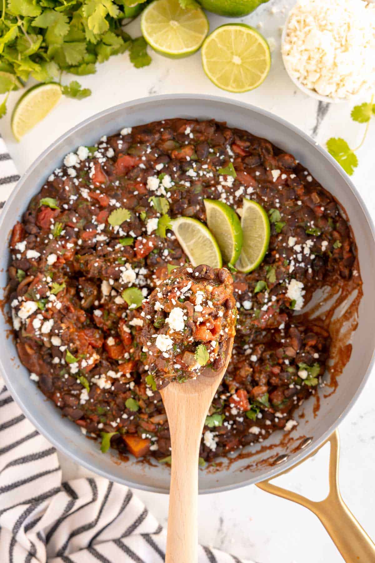 a skillet with mexican style black beans on a wooden spoon, with lime wedges.