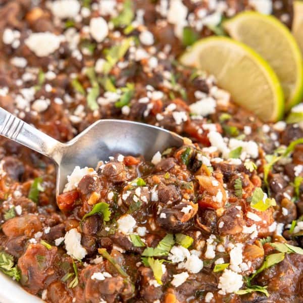 a white bowl with mexican style black beans on a spoon, with lime wedges.