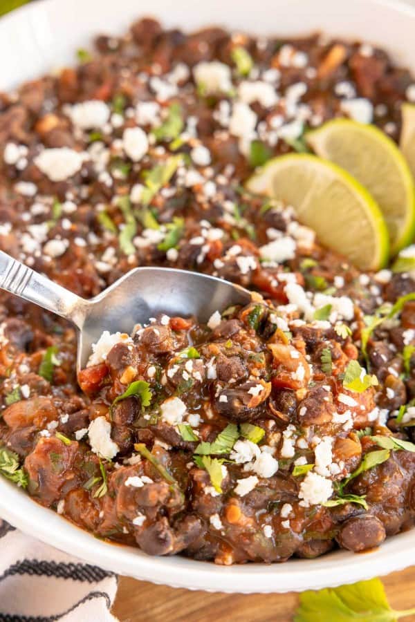 a white bowl with mexican style black beans on a spoon, with lime wedges.