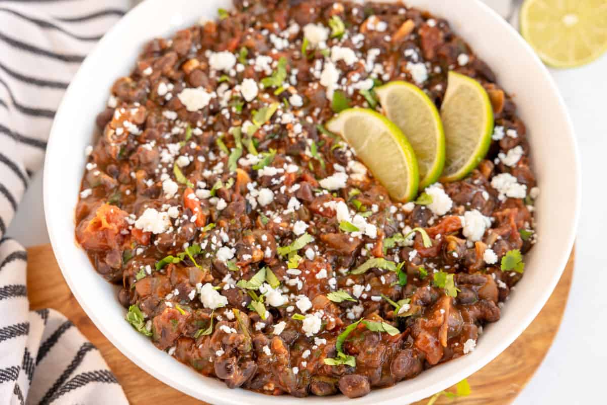 a white bowl with mexican style black beans in it, with lime wedges.