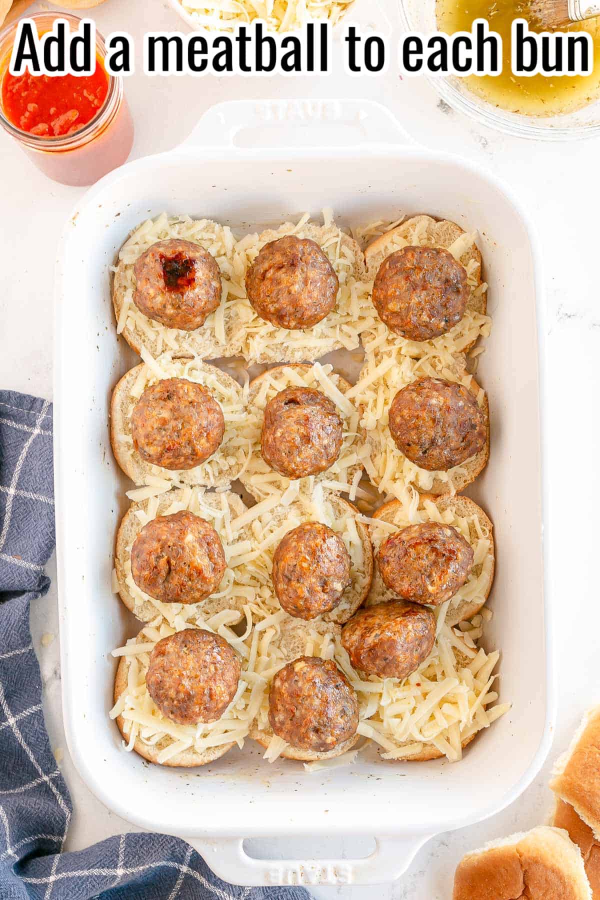 a white baking dish with slider bun bottoms, cheese and meatballs.